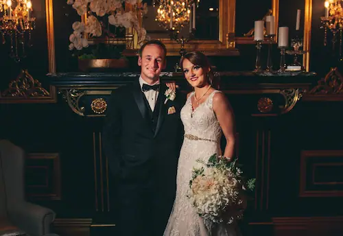 Bride and groom posing in an elegant room with chandeliers, ornate mirrors, and candlelit decor.