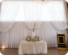Elegant sweetheart table with white drapes and gold chairs.